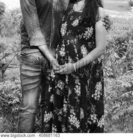 Indian Couple Posing For Maternity Baby Shoot. The Couple Is Posing In A Lawn With Green Grass And T