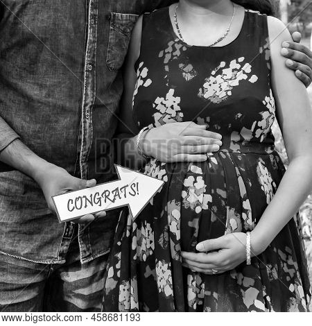 Indian Couple Posing For Maternity Baby Shoot. The Couple Is Posing In A Lawn With Green Grass And T