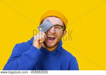 Happy Young Caucasian Guy With Credit, Debit Card In Hand Smiling Cover His Eye Ready To Spend Money