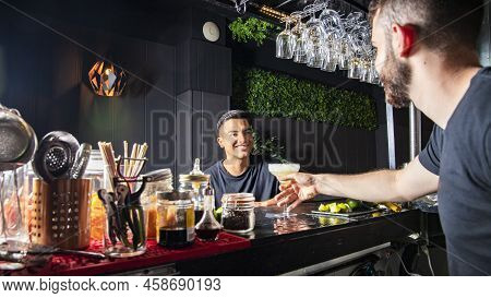 A Latin American Customer At A Bar Receives A Drink From The Waiter. Horizontal