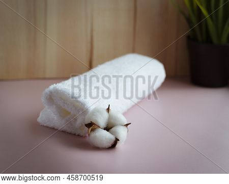 Rolled White Towel With Cotton Flower On The Pink Table With Wooden Background