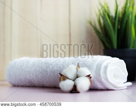 Rolled White Towel With Cotton Flower On The Pink Table With Wooden Background