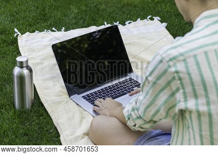 Bakc View Of Unrecognizable Young Online Using A Laptop On A Towel And Abottle Of Water On The Side