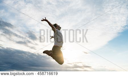 Excited Young Man In Casual Clothes Jumping High Up In The Air, Oppening His Arms Towards The Sky Ba