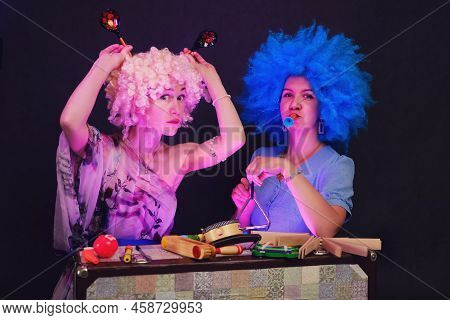 Happy Women In Funny Wigs Give A Musical Performance On A Studio Black Background. Smiling Women Sho