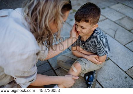 Young Mother Comforting Her Little Son And Giving Him Bandage After Getting Hurt When Fall Down In S