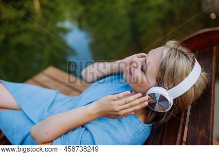 Rlaxed Woman Wearing Headphones Listening To Music Lying On A Pier By Natureal Lake In Summer