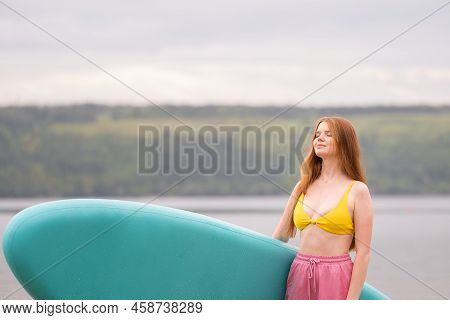 A Beautiful Girl Is Floating On A Supboard On A River. Young Woman Supsurfing At Sunrise.