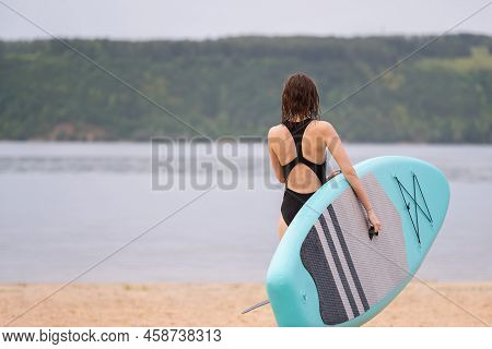 A Beautiful Girl Is Floating On A Supboard On A River. Young Woman Supsurfing At Sunrise.