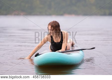 A Beautiful Girl Is Floating On A Supboard On A River. Young Woman Supsurfing At Sunrise.
