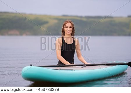 A Beautiful Girl Is Floating On A Supboard On A River. Young Woman Supsurfing At Sunrise.