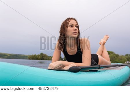 A Beautiful Girl Is Floating On A Supboard On A River. Young Woman Supsurfing At Sunrise.