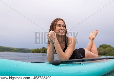 A Beautiful Girl Is Floating On A Supboard On A River. Young Woman Supsurfing At Sunrise.