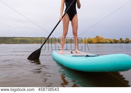 A Beautiful Girl Is Floating On A Supboard On A River. Young Woman Supsurfing At Sunrise.
