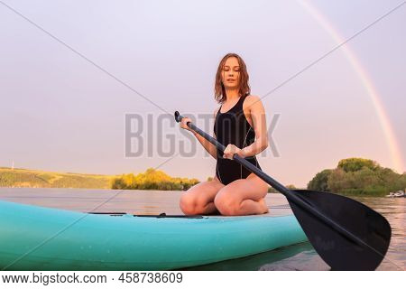 A Beautiful Girl Is Floating On A Supboard On A River. Young Woman Supsurfing At Sunrise.