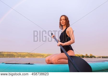 A Beautiful Girl Is Floating On A Supboard On A River. Young Woman Supsurfing At Sunrise.