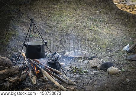 Campfire With Cooking Food In A Saucepan On A Tripod. Cooking On Fire, Camping Cooking. Living In Te