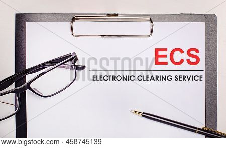 On A Light Wooden Background Glasses, A Pen And A Sheet Of Paper With The Text Ecs Electronic Cleari