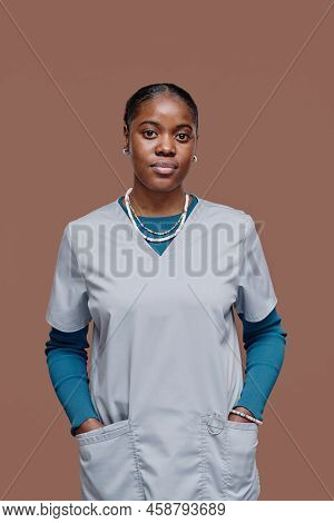 Portrait Of African Young Caregiver In Uniform Looking At Camera While Standing Against Beige Backgr
