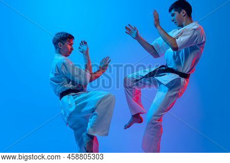 Studio Shot Of Sports Training Of Two Karatedo Fighters In Doboks Isolated On Blue Background In Neo