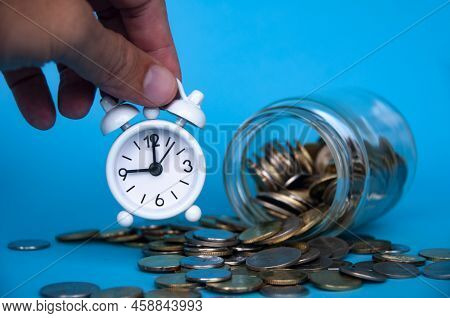 Scattered Gold Coins With Hand Holding Alarm Clock. Business And Investment Concept