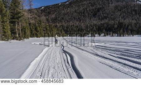 Snowmobile Tracks Are Visible On The Frozen And Snow-covered Lake. Pure White Snow All Around. A Man