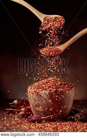 Chilli Flakes Are Poured Into A Wooden Dish. Chilli Flakes And Dried Chili Peppers On A Brown Backgr