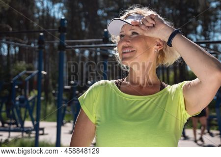 Mature Woman Wearing White Cap Sun Visor Looks Away Smiling. Young Blonde Pensioner Enjoys Healthy L