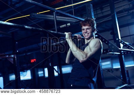 Portrait Of Sportive Muscular Young Man Training, Doing Pull Up Exrcises Isolated Over Gym Backgroun