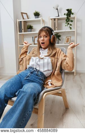 Excited Shocked Young Blonde Lady In Warm Sweater In Headphones Point Fingers Up Opening Mouth Liste