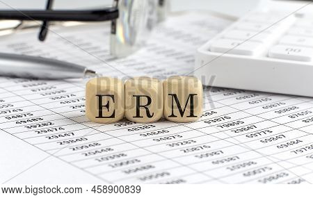 Wooden Cubes With The Word Erm On A Financial Background With Chart, Calculator, Pen And Glasses, Bu