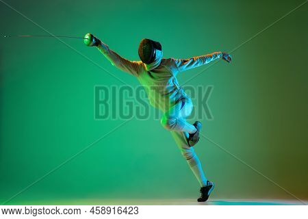 Energetic Young Man, Fencer With Smallsword Practicing Fencing Isolated On Green Background In Neon 