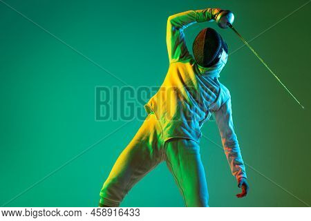 Studio Shot Of Young Man, Fencer With Smallsword Practicing Fencing Isolated On Green Background In 