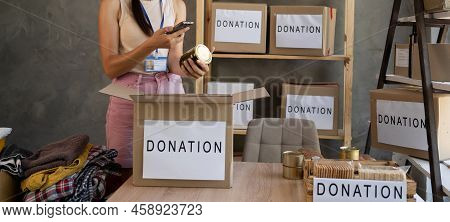 Volunteer Hands Collecting Food Into Donation Box. Working At Food Bank. Image Of Hands Packing Cans