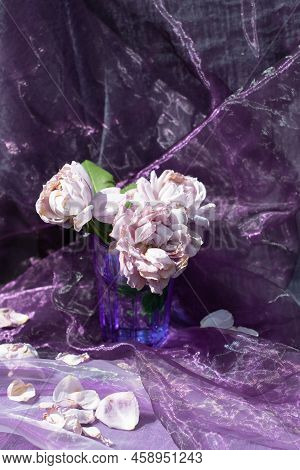 Lilac Roses In A Blue Glass On A Chair Against A Background Of Purple Chiffon