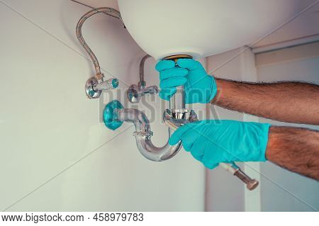 Plumber With Blue Gloves Repairing Sink Siphon In Kitchen. Plumber Repairs And Maintains Chrome Siph