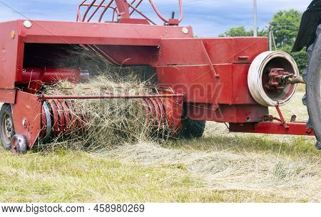 Farm Hay Field. The Process Of Harvesting Hay For Cattle, The Tractor Makes Bales In The Field.