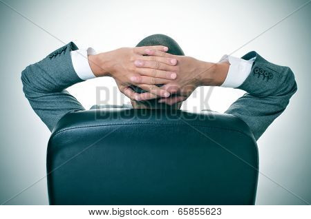 a businessman relaxing in the chair of his office with his hands behind his head