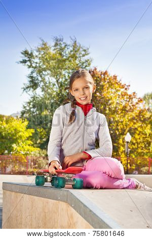 Smiling girl with braid holding red skateboard