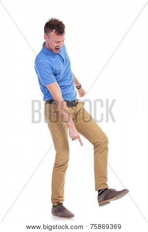full length picture of a young casual man pointing angrily at the ground while holding his foot raised, on the point of stepping on something. isolated on a white background