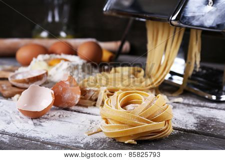 Metal pasta maker machine and ingredients for pasta on wooden background