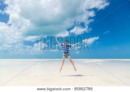 Cheerful Young Woman In Joy Jumping With Arms Out On Desert Sandy Lagoon Beach In The Caribbean