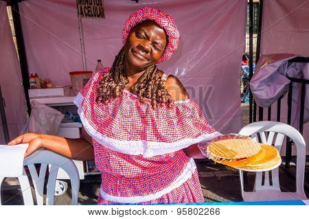 Black female wearing colorful dress and holding plate with a traditional Colombian street snack call