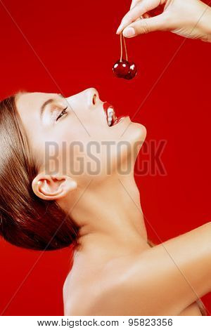 Attractive young woman eating fresh cherry. Sexual lips, red lipstick. Healthy food concept. Cosmetics. Red background.