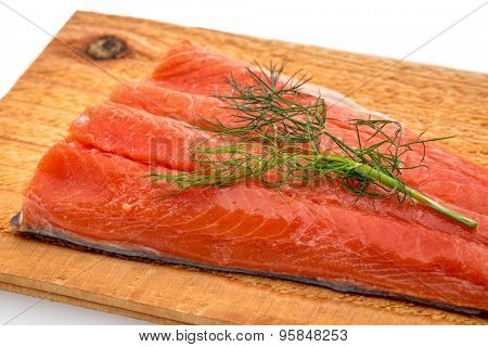a portion of sockeye salmon prepared for grilling on a water soaked cedar wood plank with green dill