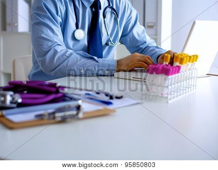 Male doctor using a laptop, sitting at his desk