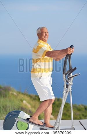 healthy senior man working out on gym treadmill machine at modern home terace with ocean view