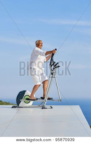 healthy senior man working out on gym treadmill machine at modern home terace with ocean view