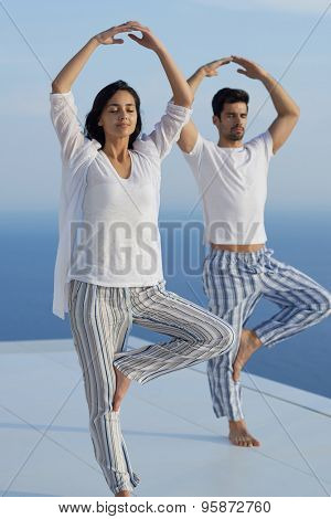 young couple practicing yoga at sunset in modern home terace with ocean and sunset in background