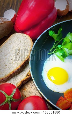 Delicious homemade omelette in vintage frypan with tomatoes, greens, bread and bell pepper on rustic wooden background, top view. Healthy breakfast with fried egg on skillet pan.